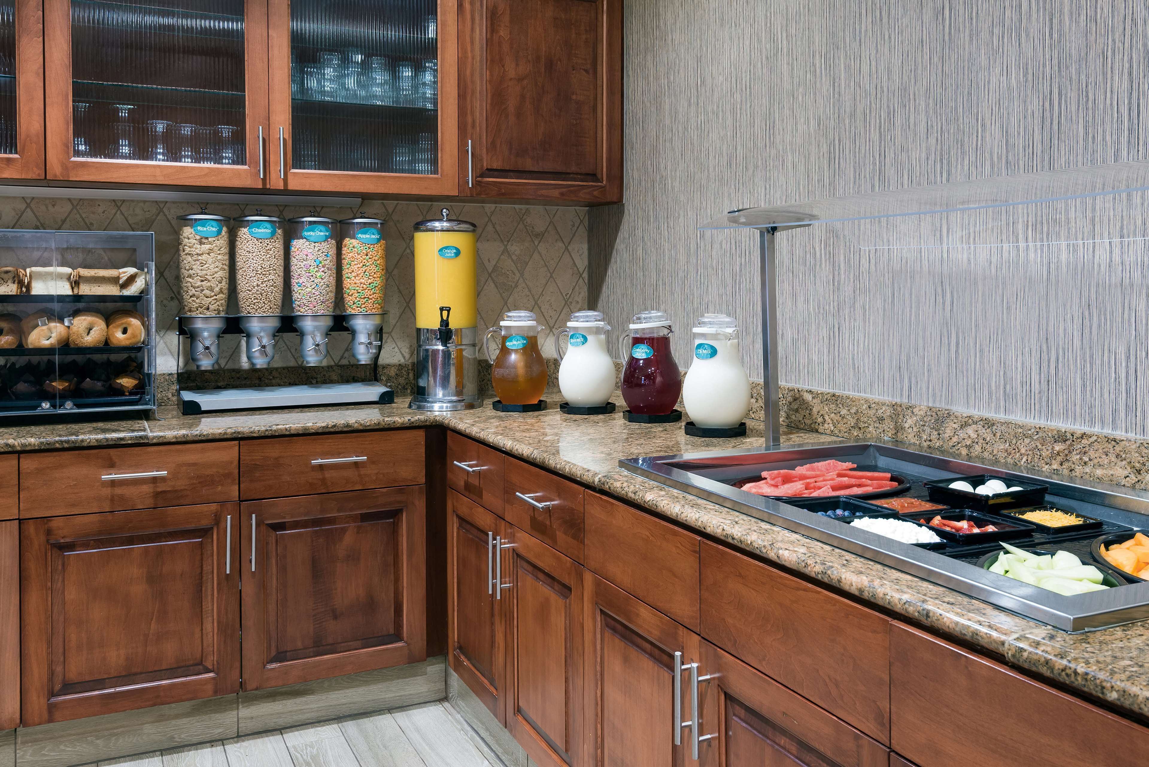 A kitchen with wooden cabinets, a granite countertop, and a variety of food items including donuts, cereal, and beverages.