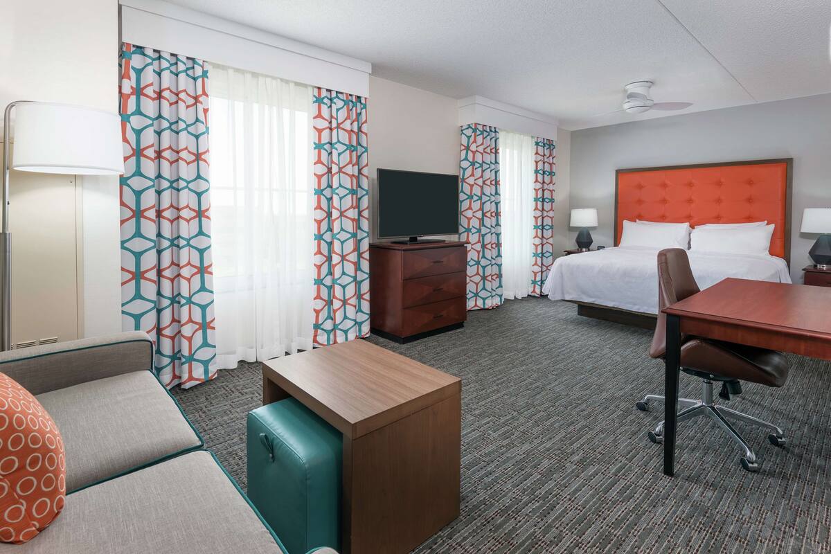 Habitación de hotel con cama, escritorio, televisión, cómoda y zona de estar.