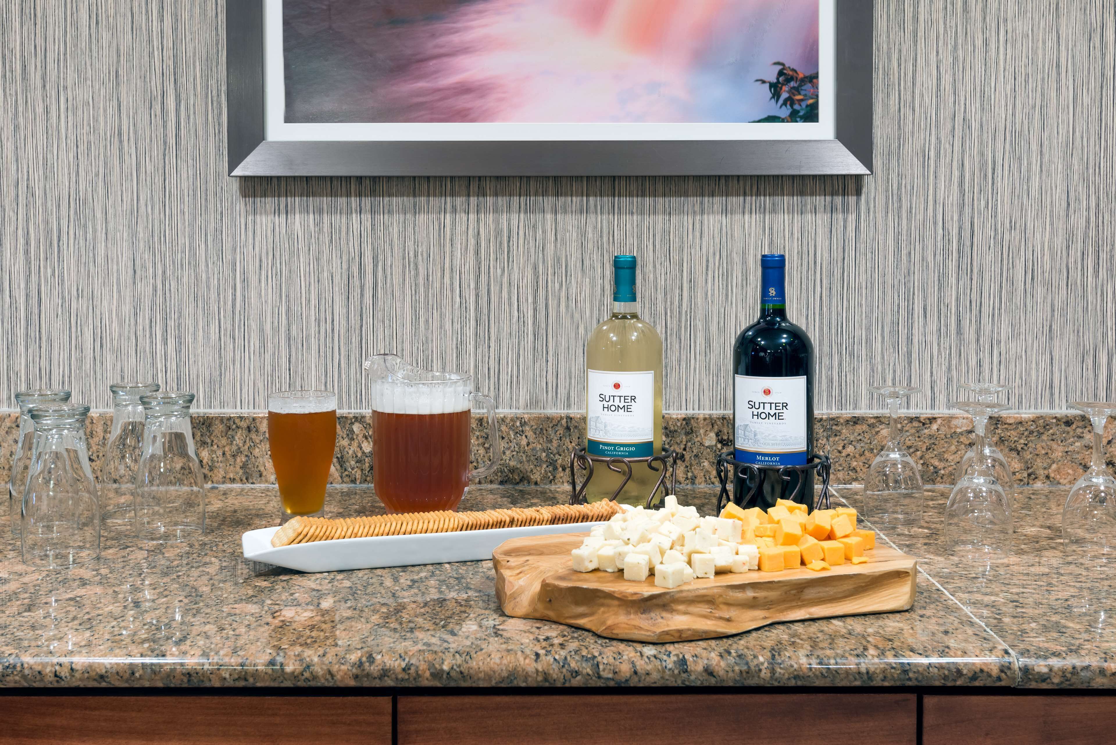 Un comptoir de cuisine avec un plateau de fromages, deux bouteilles de vin, des verres de bière et une bouteille de vin Sutter Home.