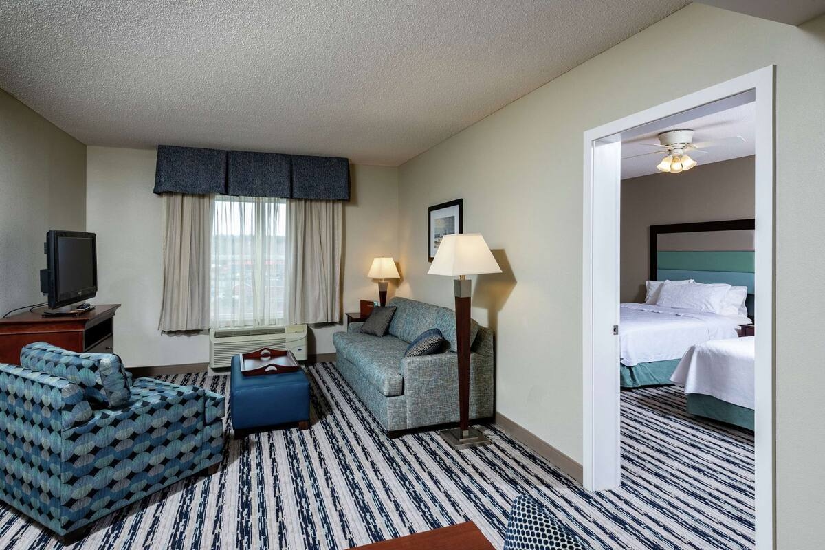 A hotel room with a sofa, a small table, a lamp, a TV, and a bed.