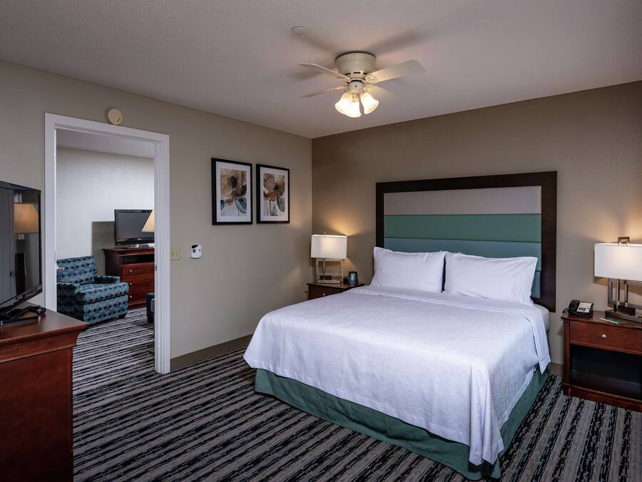 A hotel room with a bed, a desk, a television, a chair, and a ceiling fan.