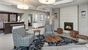 Un vestíbulo de hotel con mostrador de recepción, sillones con estampado, una mesa de centro redonda de madera y una chimenea.