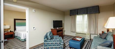 Ett hotellrum med en säng, två soffor, en tv, ett skrivbord och ett fönster med gardiner.