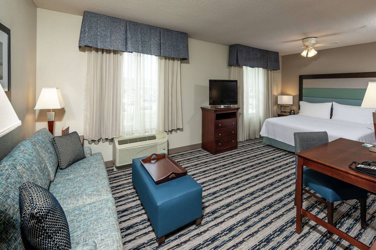 A hotel room with a bed, a sofa, a desk, a television, and a ceiling fan.