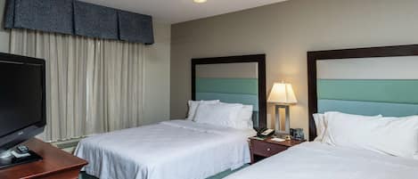 A hotel room with two beds, a television, a ceiling fan, and a nightstand with a lamp.