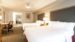 Una habitación de hotel con dos camas, un escritorio, una silla, una mesita de noche y un ventilador de techo.
