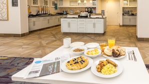 Un bufé de desayuno con gofres, huevos revueltos, salchichas y fruta.