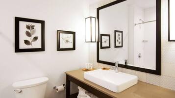 A bathroom with a toilet, sink, large mirror, framed botanical prints, and a towel rack.