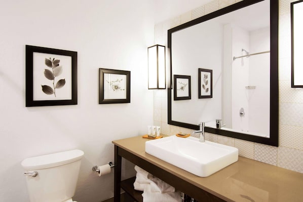 A bathroom with a toilet, sink, large mirror, framed botanical prints, and a towel rack.