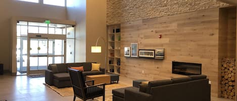 A spacious lobby with a high ceiling, a stone wall, and a fireplace. There are multiple seating areas with sofas and a coffee table.