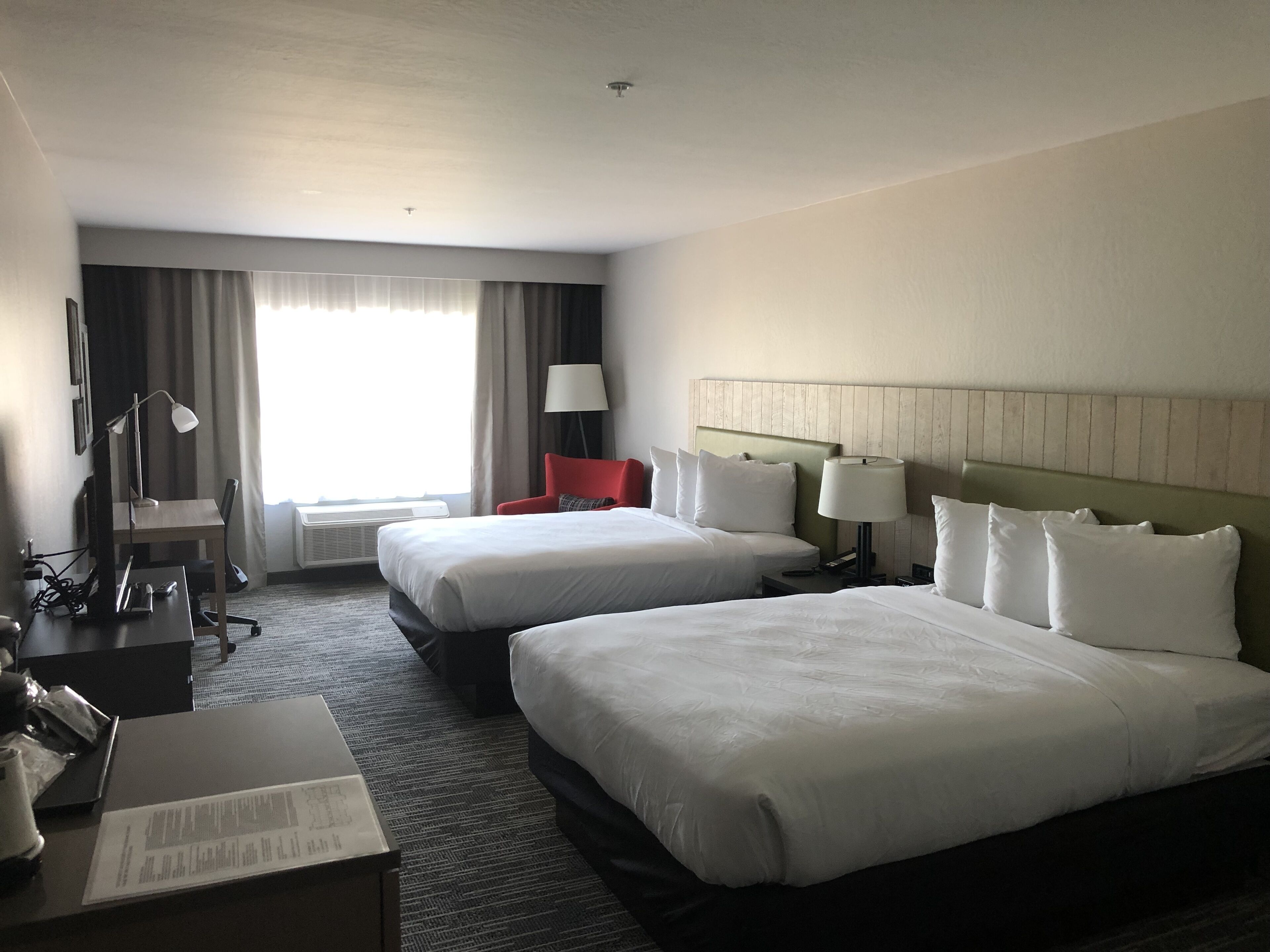 A hotel room with two beds, a desk, a chair, a lamp, and a window with curtains.