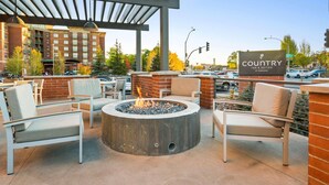 A patio area with outdoor seating and a fire pit, overlooking a street and a hotel building.