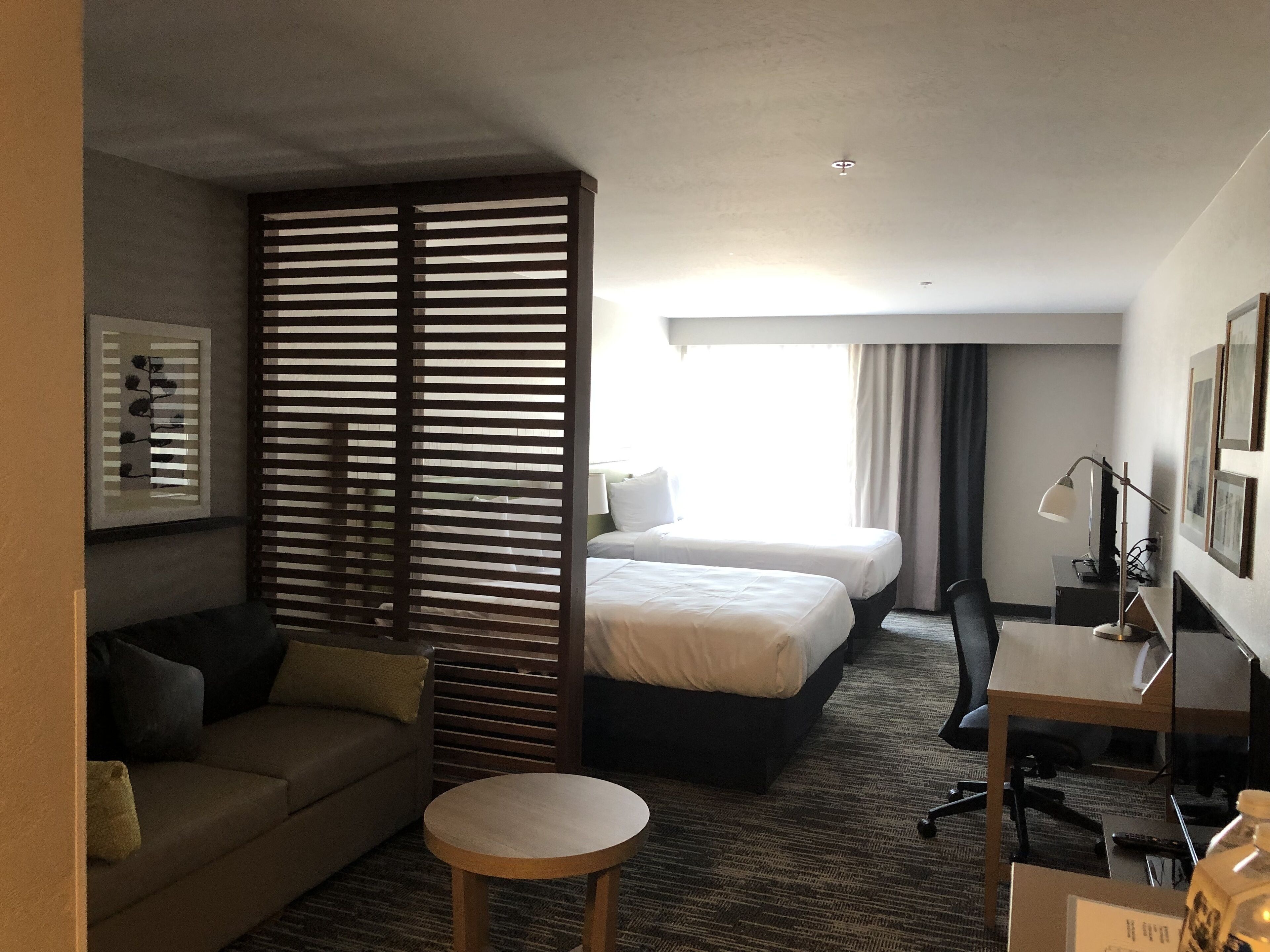 A hotel room with a bed, a desk, a chair, a small table, a sofa, and a decorative partition.