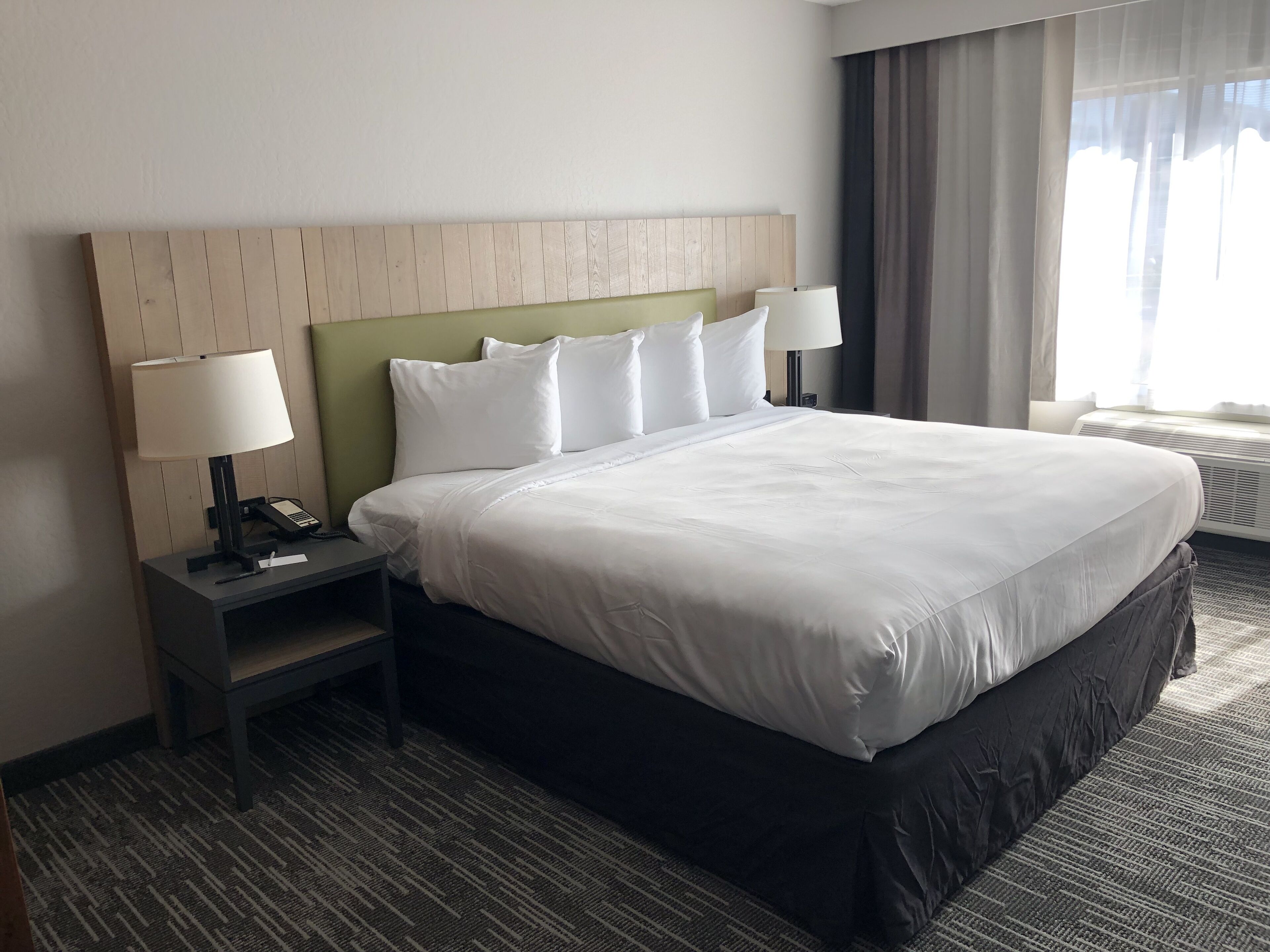 A hotel room with a large bed, a nightstand with a lamp, a telephone, and a window with curtains.