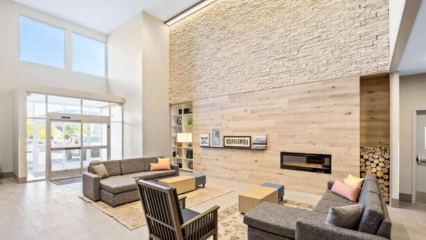 A spacious lobby with a high ceiling, a stone wall, and a fireplace. There are multiple seating areas with sofas and a wooden chair.