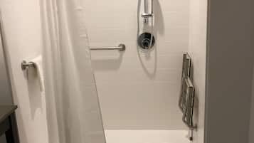 Un espace douche avec un rideau blanc, une douchette à main et un robinet fixé au mur.