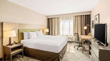 A hotel room with a large bed, a desk, a chair, a television, and a lamp.
