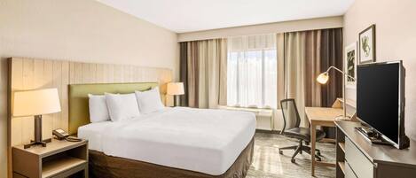 A hotel room with a large bed, a desk, a chair, a television, and a lamp.