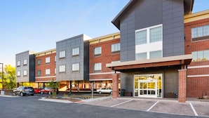 A multi-story hotel with a modern design, featuring a mix of brick and grey exterior walls, large windows, and a covered parking area.