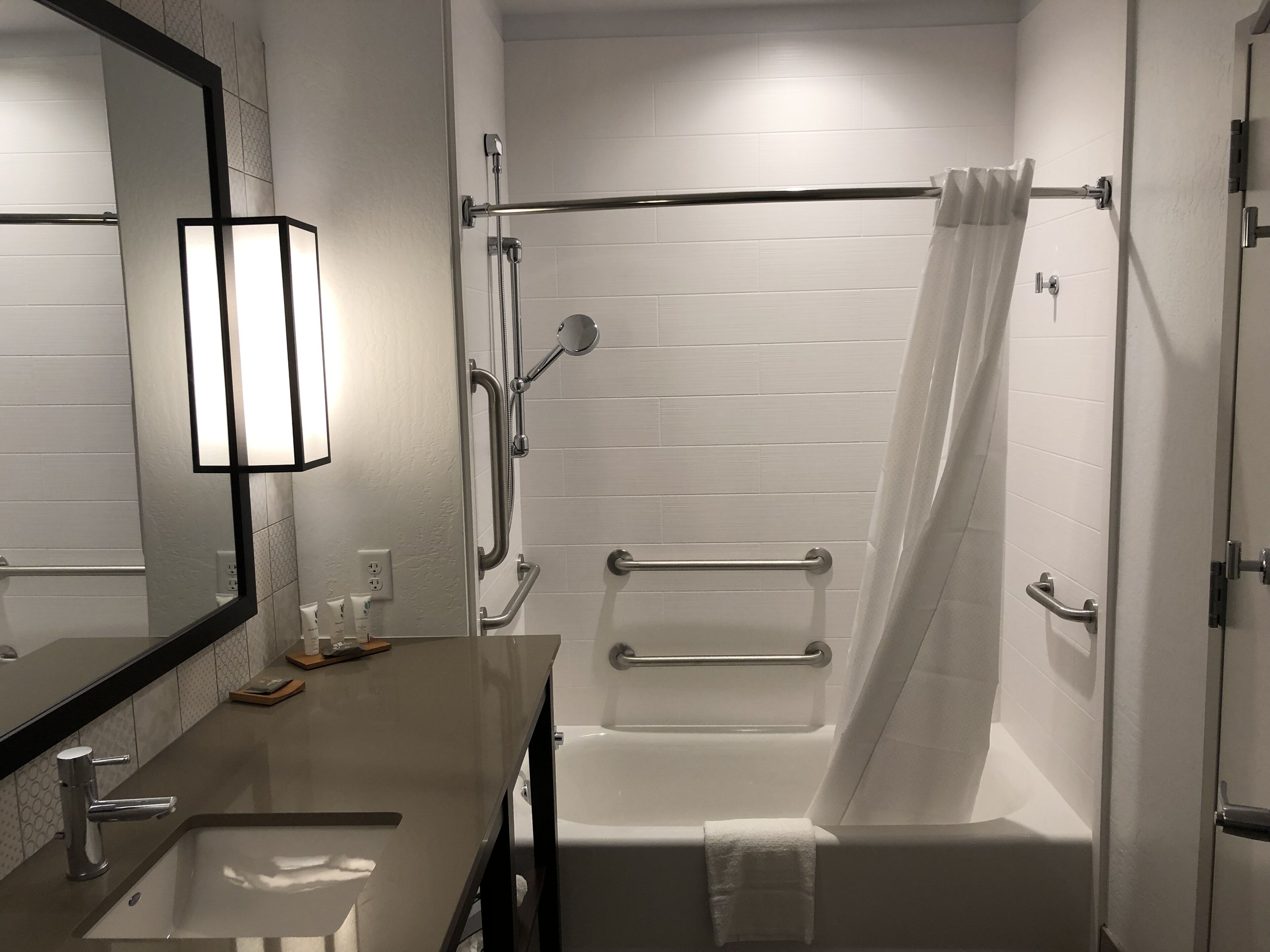 A modern bathroom with a sink, mirror, shower with grab bars, and a bathtub.