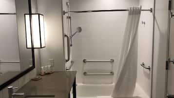 Un baño moderno con lavamanos, espejo, ducha con barras de apoyo y bañera.
