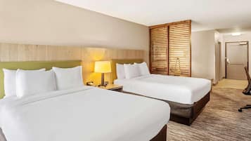 A hotel room with two beds, a wooden headboard, a nightstand with a lamp, and a door.