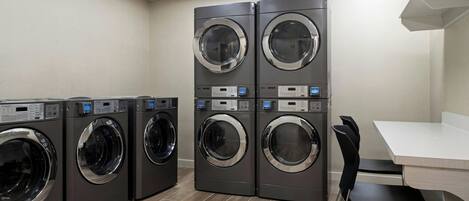A laundry room with four stacked front-loading washers and dryers, a white table, and black chairs.