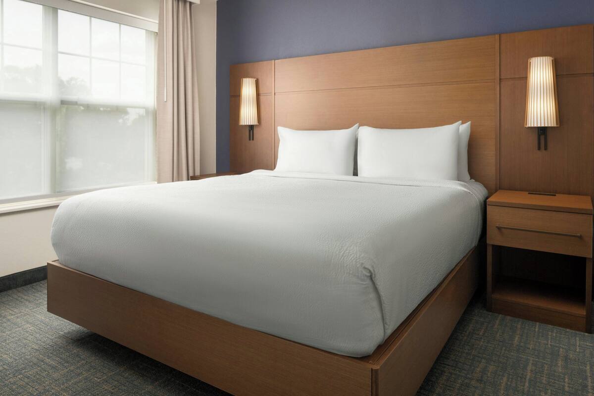 A modern hotel room with a large bed, two bedside tables, and a window with curtains.