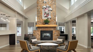 A spacious living area with a stone fireplace, comfortable seating, and a large window providing natural light. - Residence Inn Atlantic City Airport Egg Harbor Township (Egg Harbor Township)