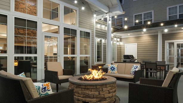 An outdoor patio with wicker furniture, a stone fire pit, and string lights. - Residence Inn Atlantic City Airport Egg Harbor Township (Egg Harbor Township)