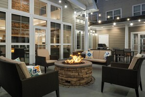 Un patio al aire libre con mobiliario de mimbre, un hogar de piedra y luces colgantes.