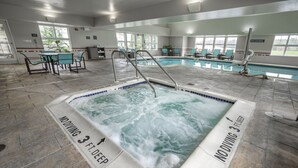 Une piscine intérieure avec un jacuzzi, entourée de chaises longues et dotée d’un sol carrelé.