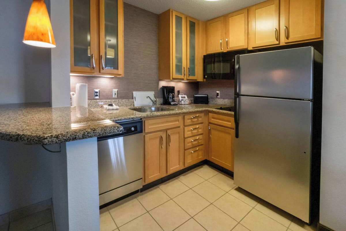 A modern kitchen with granite countertops, stainless steel appliances, wooden cabinets, and a built-in dishwasher.