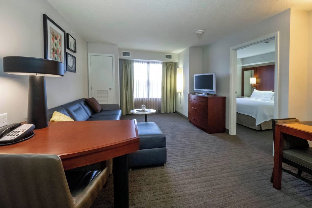 A hotel room with a sofa, a small table, a desk with a telephone, a television on a dresser, and a bed.