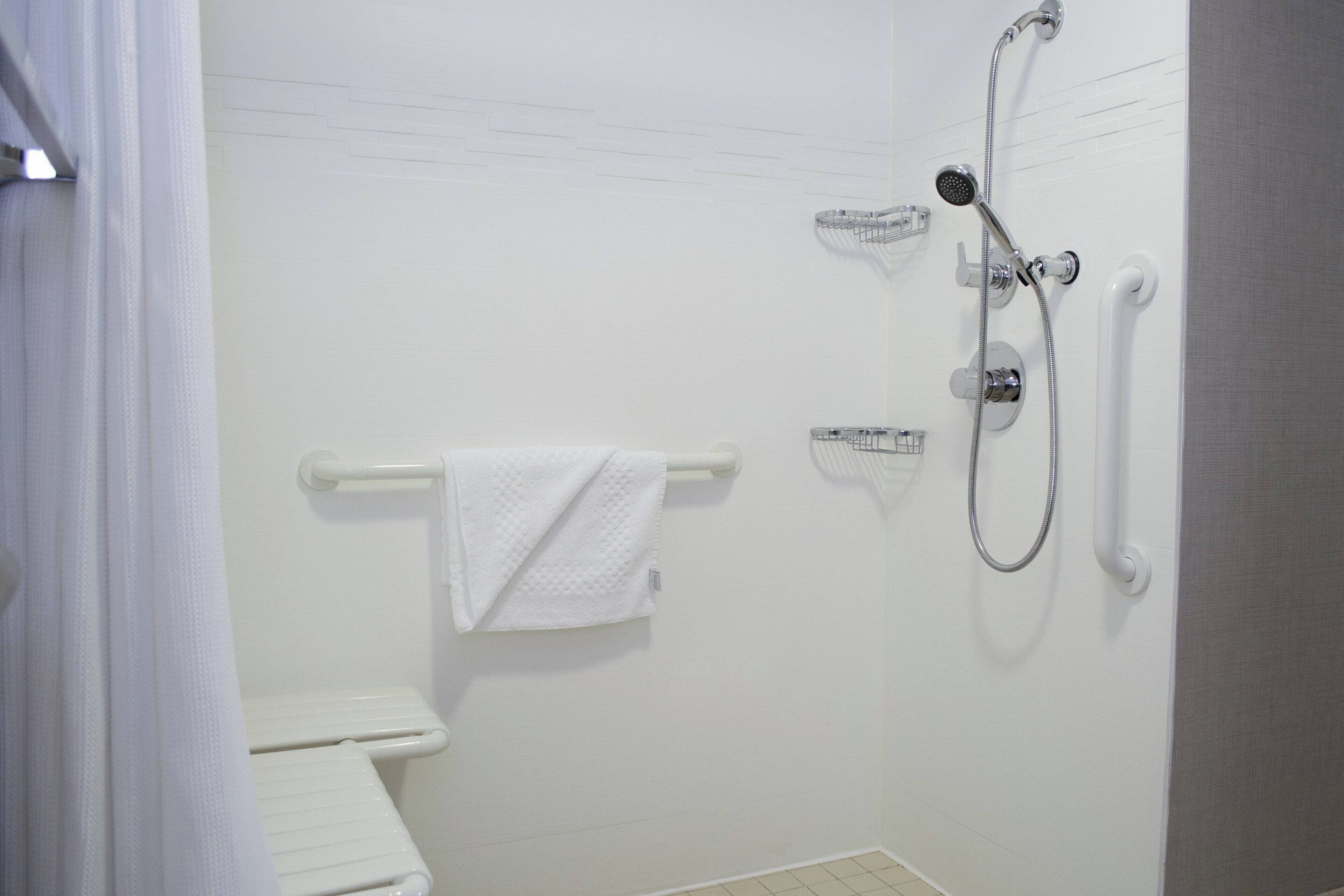 Ein Badezimmer mit Toilette, Handtuchhalter mit Handtuch, Dusche mit Duschbrause und einer Haltestange.