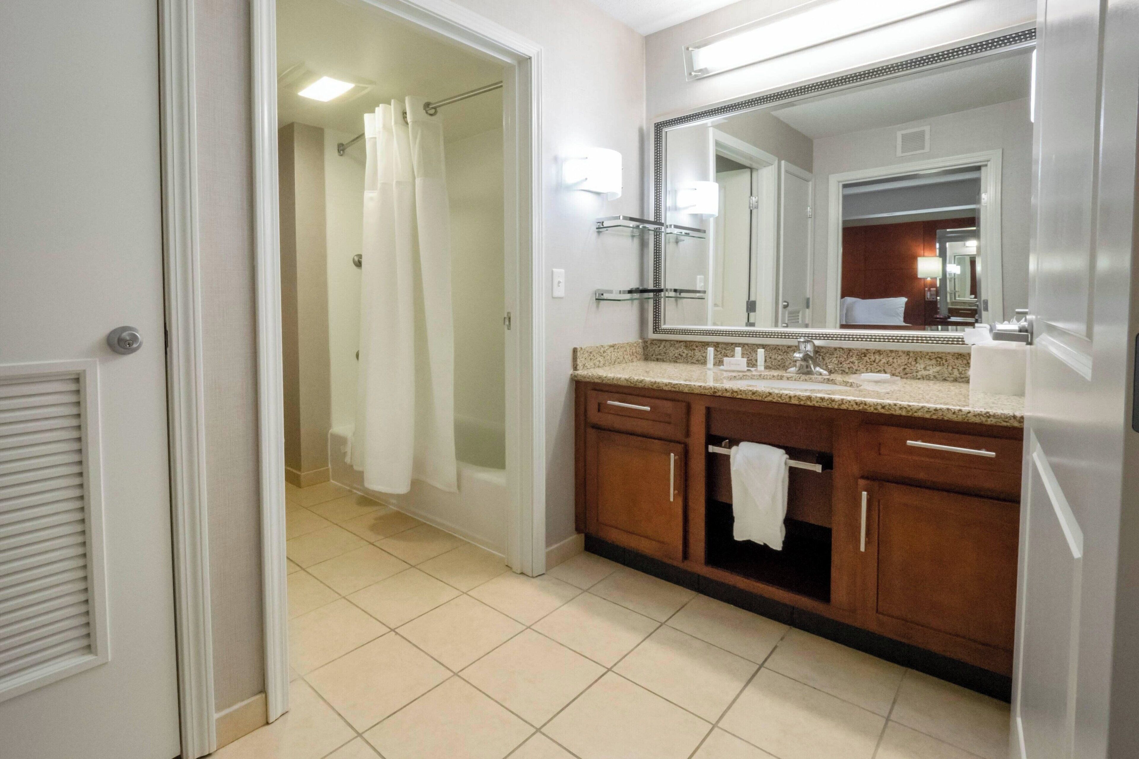A bathroom with a shower, a sink with a mirror, and wooden cabinets.