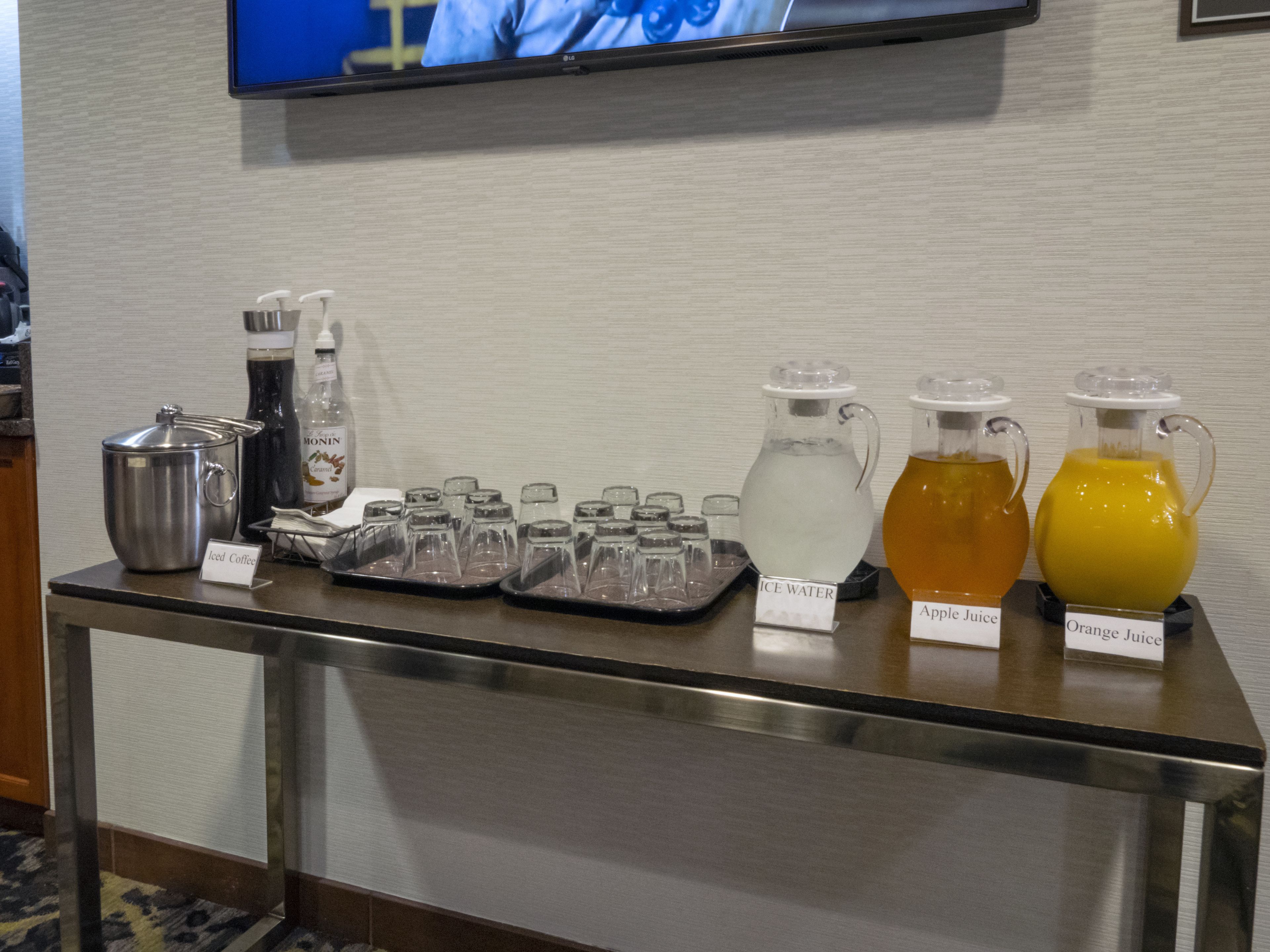 A buffet table with iced coffee, ice water, apple juice, and orange juice.