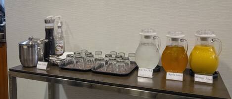 A buffet table with iced coffee, ice water, apple juice, and orange juice.