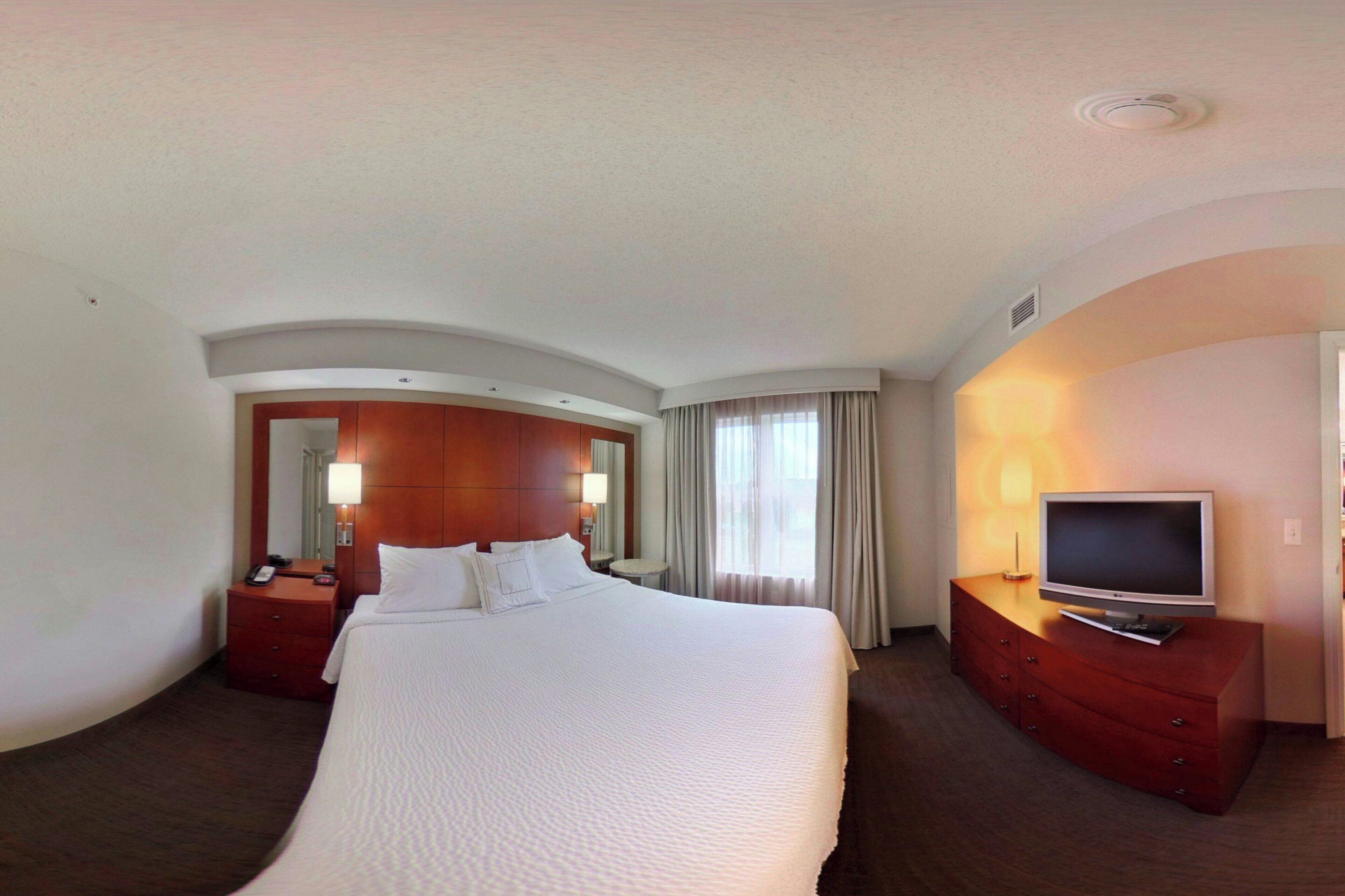 A hotel room with a large bed, a TV on a wooden dresser, a mirror, and a door leading to another room.