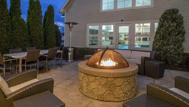 Une terrasse extérieure avec un foyer en pierre, des meubles en osier et une piscine visible à travers les fenêtres.