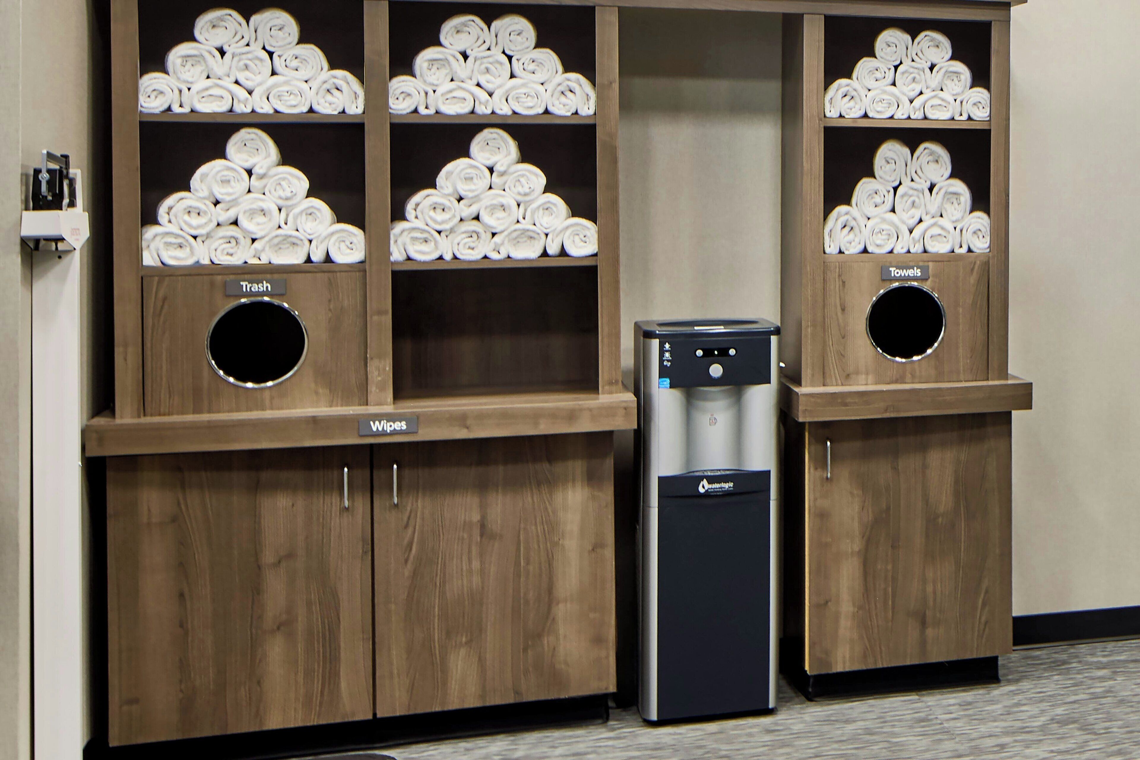 A hotel room with a wooden cabinet containing neatly rolled towels and a water dispenser.