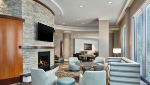 A hotel lobby with a stone fireplace, comfortable seating, a flat-screen TV, and large windows. - Residence Inn National Harbor Washington, DC Area (Oxon Hill)