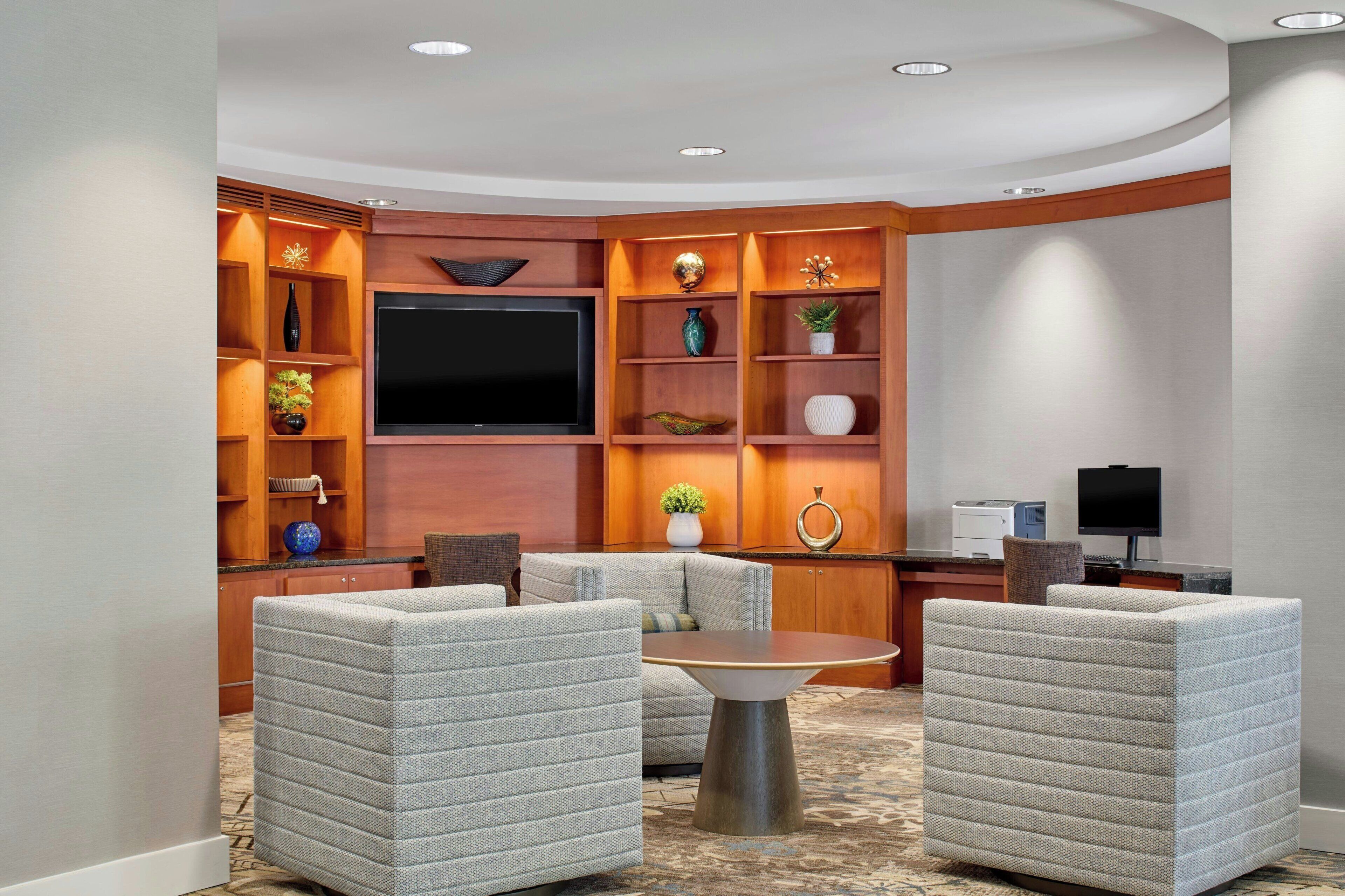 A modern living room with a flat-screen TV, built-in shelving with decorative items, and a seating area with a round coffee table.