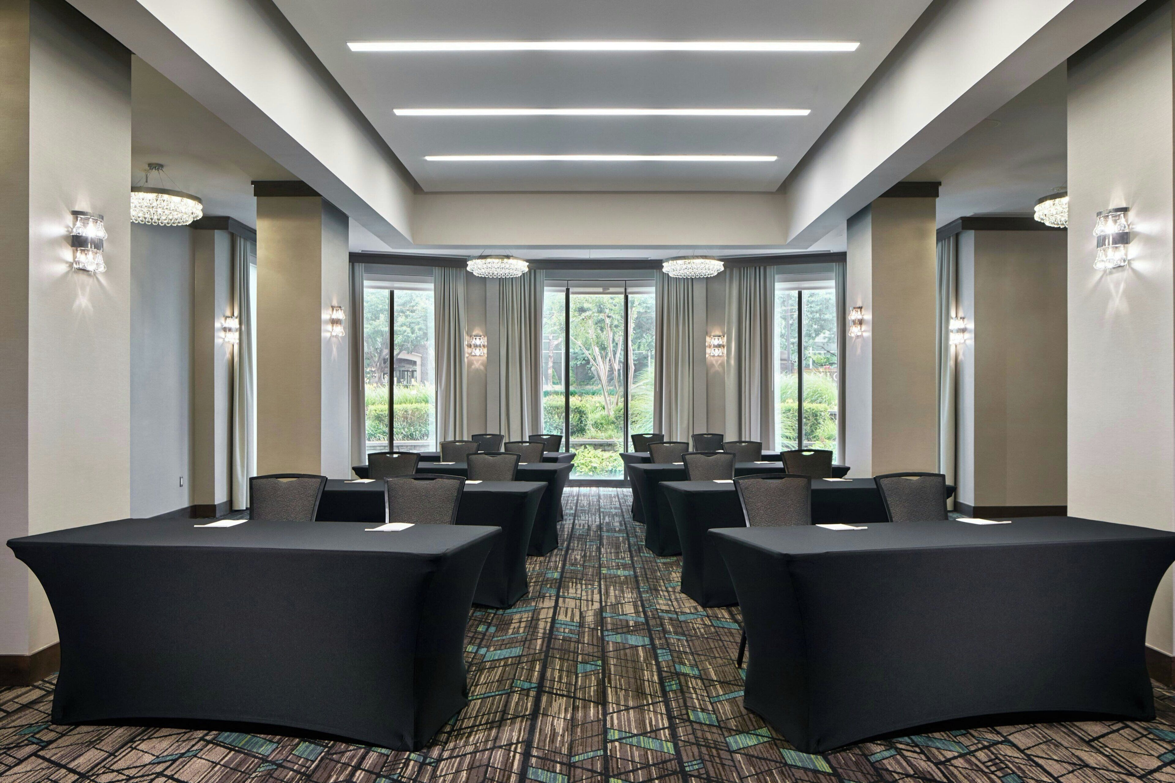 A conference room with tables, chairs, chandeliers, and large windows.
