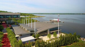 A modern building with a flat roof and large windows, situated near a body of water with a dock and an American flag. - Residence Inn National Harbor Washington, DC Area (Oxon Hill)