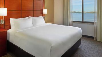 Habitación de hotel con una cama grande, cabecera de madera, dos lámparas de noche, vista a un cuerpo de agua a través de una ventana y piso alfombrado.