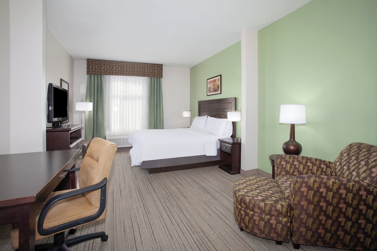 A hotel room with a bed, a desk, a chair, a TV, and a lamp.