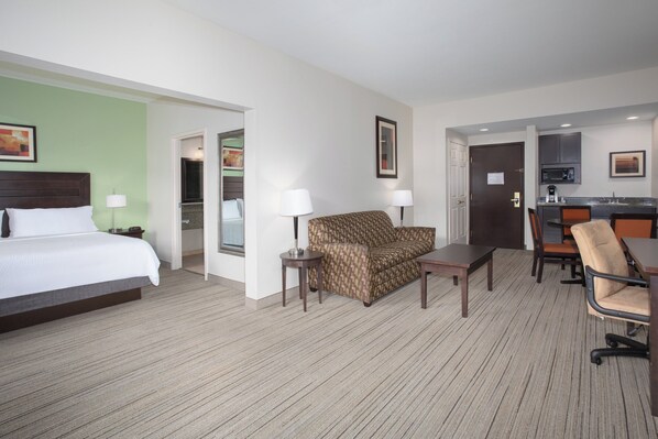 A hotel room with a bed, a sofa, a small table, a chair, and a kitchenette area. - Holiday Inn Express & Suites Oro Valley-Tucson North by IHG (Oro Valley)