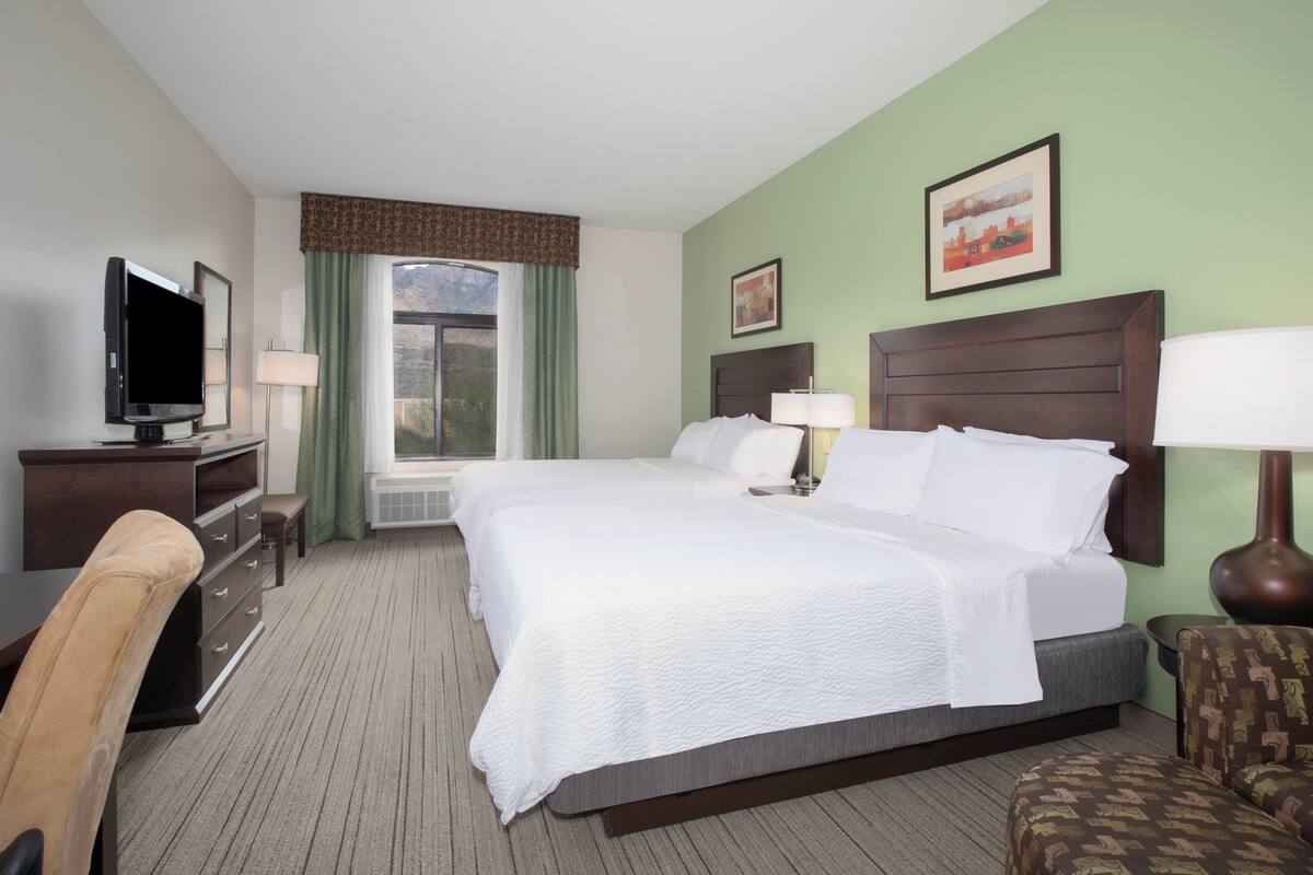 A hotel room with two beds, a TV, a desk, and a chair.