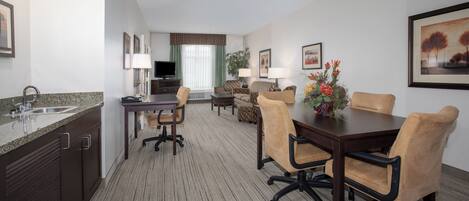 A hotel room with a kitchenette, dining area, and a living space.